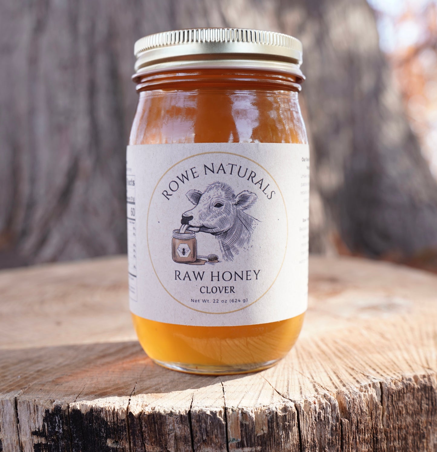 Jar of Rowe Naturals Raw Honey on a wooden surface with a blurred natural background