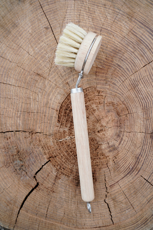 A wooden-handled cleaning brush with natural sisal bristles placed on a rustic wood log background.