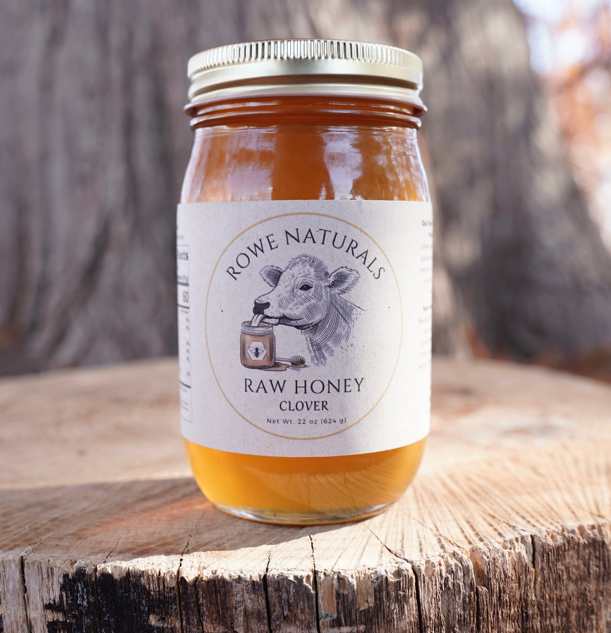 Jar of Rowe Naturals Raw Honey on a wooden surface with a blurred natural background