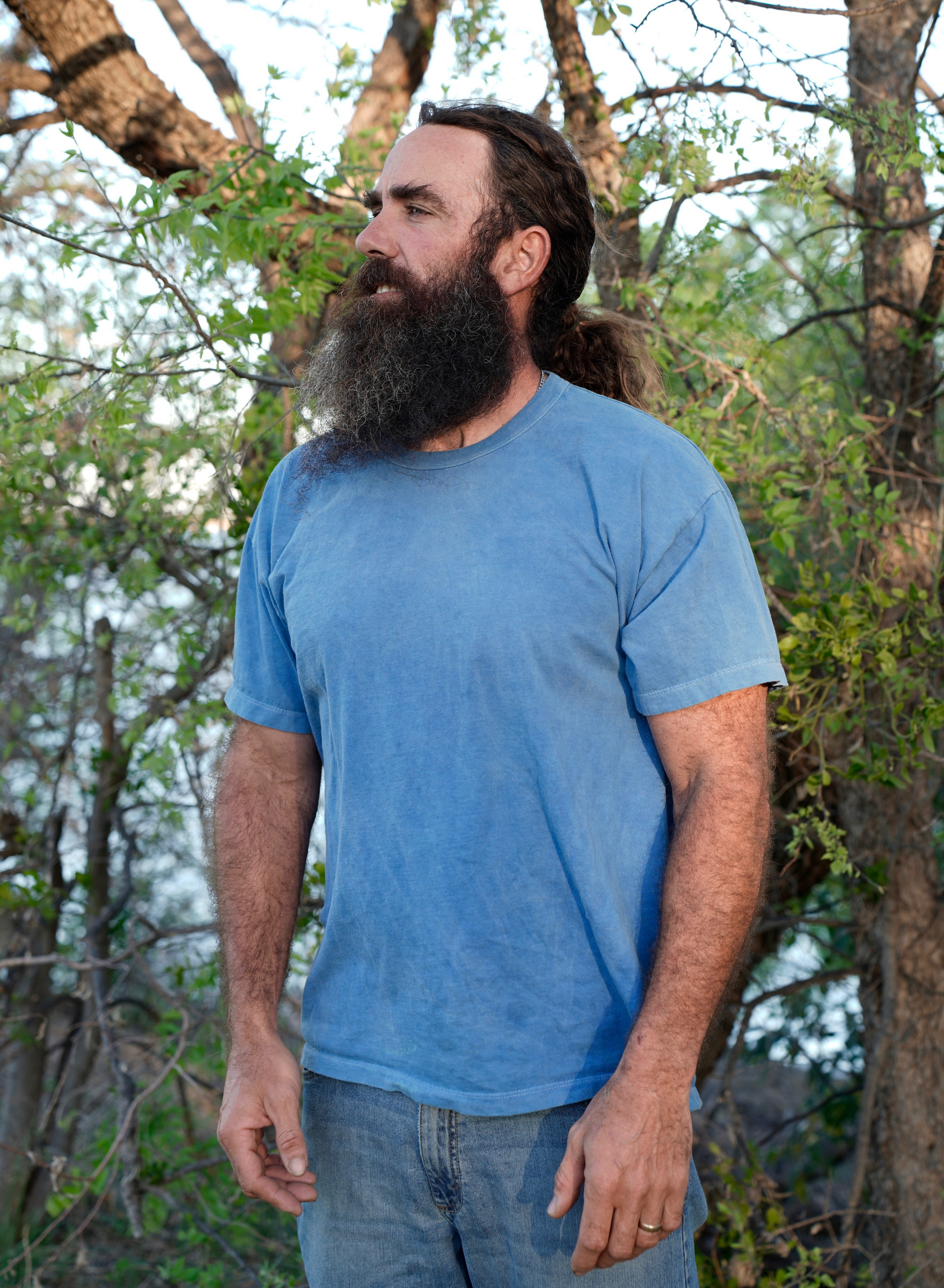 Man with a beard wearing a organic cotton blue t-shirt standing in a forested area